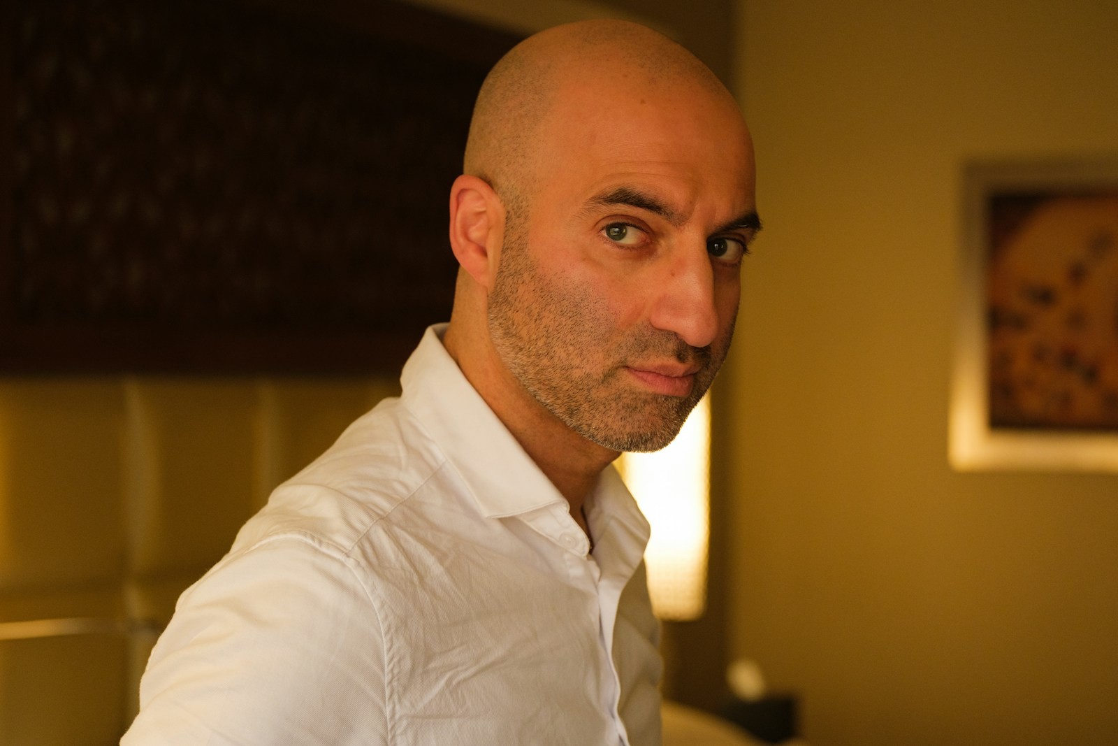 Bald man in a white shirt looking at the camera.