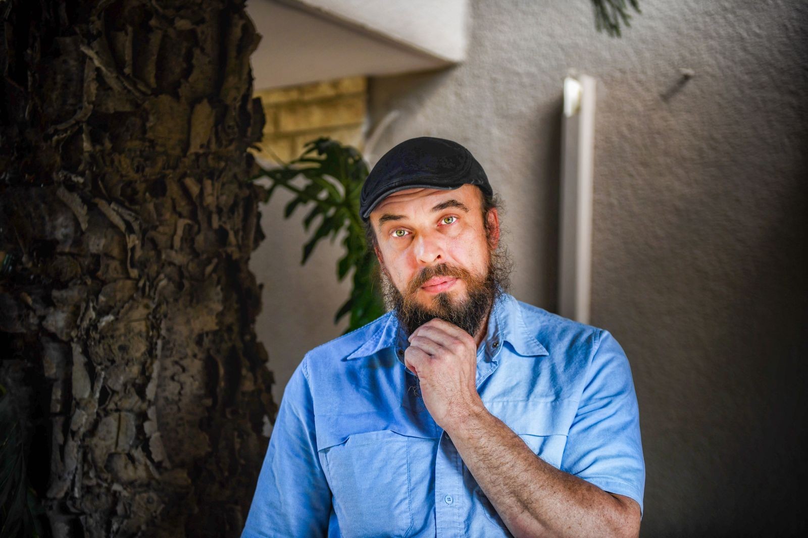 Adult man with beard and cap posing thoughtfully outdoors.